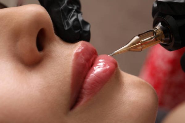 Young woman undergoing procedure of permanent lip makeup in tattoo salon, closeup